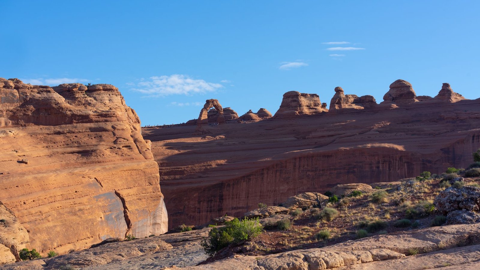 A wide red-rock slickrock overlook near Moab with distant sandstone fins and canyon country stretching to the horizon under a clear blue sky